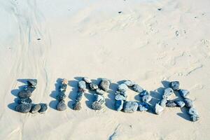 el palabra linda es hecho de rocas en el playa foto