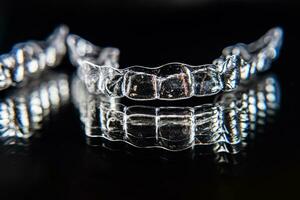 Invisible dental teeth brackets tooth aligners on black background. Plastic braces dentistry retainers to straighten teeth. photo