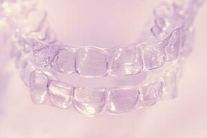Invisible dental teeth brackets tooth aligners on pink background. Plastic braces dentistry retainers to straighten teeth. photo