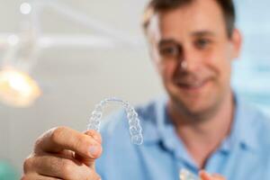 A smiling dentist doctor holds transparent aligners in his hands photo