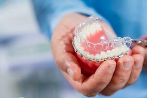 Dental care.Smiling orthodontist doctor holding aligners and braces in hand shows the difference between them photo