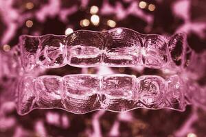 Invisible aligner teeth retainers on a pink background photo