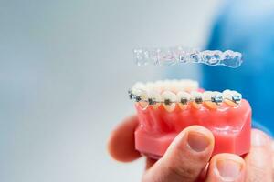 Dental care.Smiling orthodontist doctor holding aligners and braces in hand shows the difference between them photo