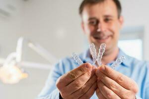 A smiling dentist doctor holds transparent aligners in his hands photo