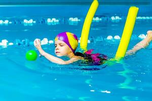 A little boy with a life jacket on his chest learns to swim in an indoor pool. photo