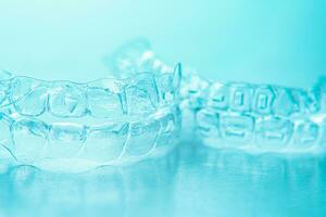 Invisible dental teeth brackets tooth aligners on turquoise background. Plastic braces dentistry retainers to straighten teeth. photo