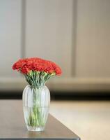 The scarlet flowers were placed in a glass vase on the table. The background image was blurred, making the flowers stand out. photo