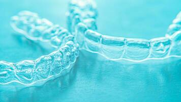 Invisible dental teeth brackets tooth aligners on turquoise background. Plastic braces dentistry retainers to straighten teeth. photo