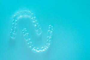 Invisible dental teeth brackets tooth aligners on turquoise background. Plastic braces dentistry retainers to straighten teeth. photo