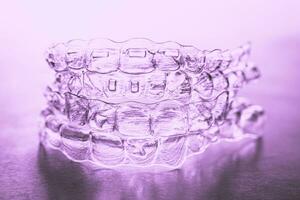 Invisible dental teeth brackets tooth aligners on pink background. Plastic braces dentistry retainers to straighten teeth. photo