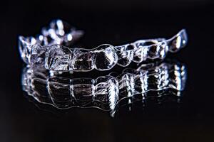 Invisible dental teeth brackets tooth aligners on black background. Plastic braces dentistry retainers to straighten teeth. photo