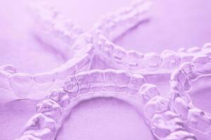 Invisible dental teeth brackets tooth aligners on pink background. Plastic braces dentistry retainers to straighten teeth. photo