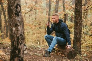 un hombre viajero en el otoño bosque descansa en un detener y bebidas té. foto