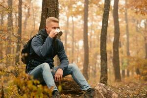 chico viajero en el otoño bosque descansa en un detener y bebidas té. foto