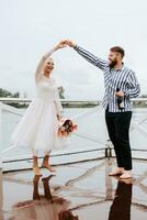 Young newlyweds dance barefoot and have fun on the pier by the water. photo