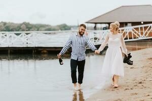 Young spouses go along the beach line barefoot and hold hands. photo