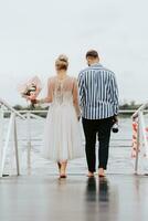 The newlyweds on the pier. The bride and groom go barefoot along the wharf. photo