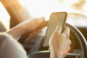 un hombre se sienta en un coche y mira a su teléfono con el navegador aplicación en un soleado día foto