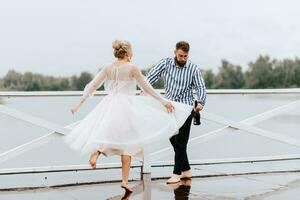 joven recién casados danza descalzo y tener divertido en el muelle por el agua. foto