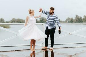 joven recién casados danza descalzo y tener divertido en el muelle por el agua. foto