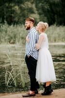 The bride gently hugs the groom from behind on the shoreline. Beautiful newlyweds on the background of the river. photo