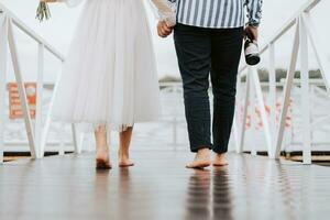 Feet of the newlyweds on the background of the pier.The bride and groom go barefoot along the wharf. photo