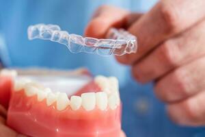 Close-up. The doctor puts transparent aligners on the teeth of the artificial jaw photo