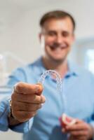 Dental care.Smiling orthodontist doctor holding aligners and braces in hand shows the difference between them photo