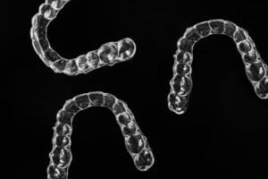 Invisible dental teeth brackets tooth aligners on black background. Plastic braces dentistry retainers to straighten teeth. photo