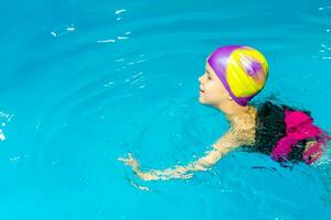 un pequeño chico con un vida chaqueta en su cofre aprende a nadar en un interior piscina. foto