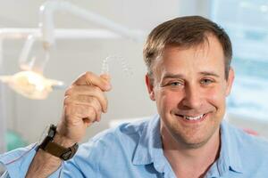 A smiling dentist doctor holds transparent aligners in his hands photo