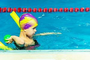 un pequeño chico con un vida chaqueta en su cofre aprende a nadar en un interior piscina. foto