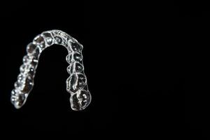 Invisible dental teeth brackets tooth aligners on black background. Plastic braces dentistry retainers to straighten teeth. photo