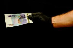 a person in black gloves holding a twenty euro bank note photo