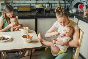 Two tired but happy mothers feed their babies milk porridge in the kitchen photo