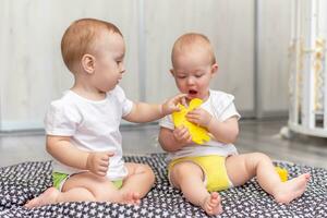 Cute happy kids play together on the floor with toys and take them into mouth photo