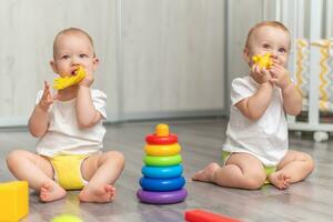 Cute happy kids play together on the floor with toys and take them into mouth photo