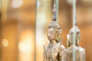 Deity statue standing straight made of brass, wearing gold costume with Chada on top of his head in a luxury wood mirror closet. photo