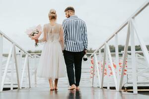 The newlyweds on the pier. The bride and groom go barefoot along the wharf. photo