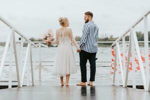 The newlyweds on the pier. The bride and groom go barefoot along the wharf. photo