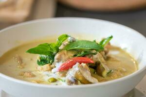 Close up to Green Curry with Chicken garnished on top with pepper and basil was served with white bowl put on wicker cream color placemat. photo