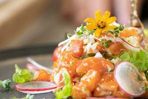 primer plano ensalada de salmón crudo picante estilo comida tailandesa decorada con piel de pescado frito crujiente y flor amarilla en la parte superior y microhierba alrededor del plato. listo para servir y comer. foto