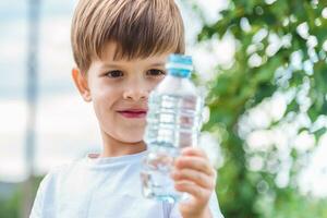 joyful child drinks clear water from a bottle on a sunny day in nature photo