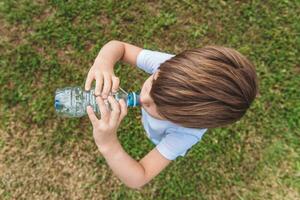 Cute child drinks water from a bottle on the street in summer photo