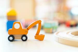 An orange wooden toy excavator is placed on the table in front of other blurry wooden toys. photo