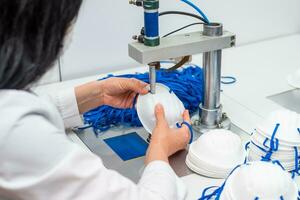 The girl works in a factory for the production of medical masks with nanofibre and solder loops with ultrasound on a machine. Coronavirus and Covid-19 Protection.Close-up. photo