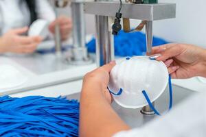 A woman works at a machine for the manufacture of medical masks with nanofibre and solder loops to them with ultrasound. Coronovirus and Covid-19 Prevention photo