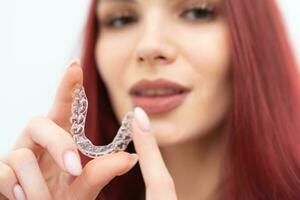 A woman with a beautiful smile holds aligners in her hand photo