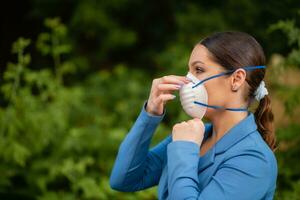 Beautiful girl puts a medical mask on her face on the nature. Coronavirus and Covid-19 Protection photo