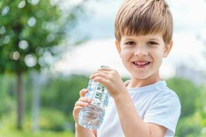 alegre niño bebidas claro agua desde un botella en un soleado día en naturaleza foto